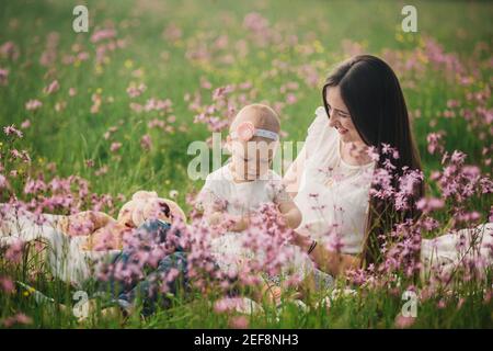 la mamma giovane e la bambina carina camminano e giocano sul campo con fiori selvatici. la famiglia si diverte in estate, giorno di sole. infanzia e parentismo Foto Stock