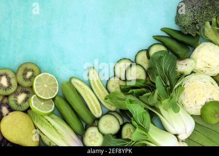 Cibo verde ad alta fibra per il concetto di salute digestiva con frutta e verdura su bordo blu di sfondo chiazzato. Foto Stock