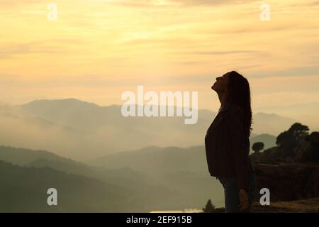 Vista laterale ritratto di una silhouette donna che respira aria fresca in montagna al tramonto Foto Stock