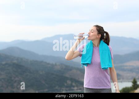 Buon corridore che beve acqua dalla bottiglia di plastica dopo lo sport dentro la montagna Foto Stock