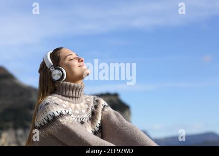 Donna felice rilassarsi ascoltando la musica con le cuffie wireless in la montagna in inverno Foto Stock