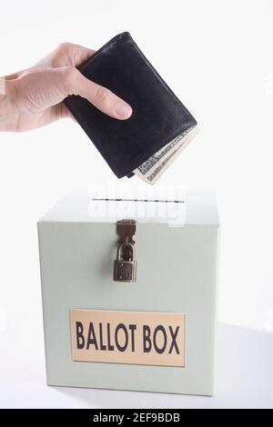 Primo piano di una personÅ½s mano che mette soldi pieni di portafoglio in una scatola di votazione Foto Stock
