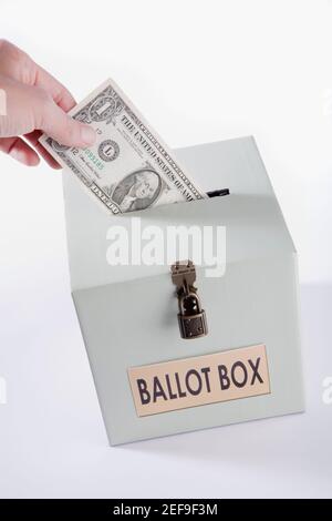 Close up di una personÅ½s mano che inserisce una fattura in dollari USA in una scatola di votazione Foto Stock