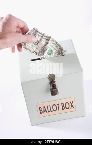 Close up di una personÅ½s mano che inserisce una fattura in dollari USA in una scatola di votazione Foto Stock