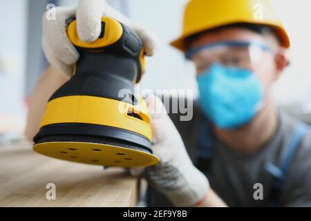 Il costruttore principale nella maschera protettiva sta tenendo la levigatrice a disco Foto Stock