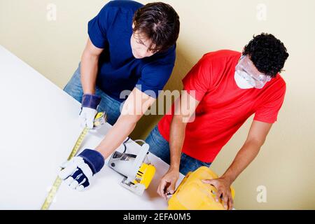 Misurazione uomo medio con un nastro di misurazione e un giovane uomo che apre una cassetta degli attrezzi Foto Stock