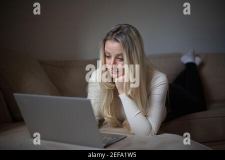 Una ragazza attraente lavora con il suo laptop da casa durante la pandemia del coronavirus Foto Stock