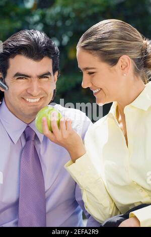 Donna d'affari che alimenta una mela verde ad un uomo d'affari e sorridente Foto Stock