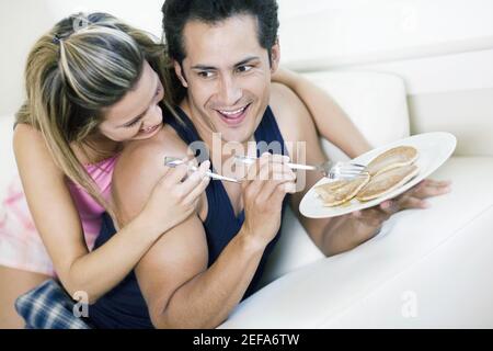 Giovane che tiene un piatto di frittelle con un giovane donna stesa su di lui e sorridente Foto Stock