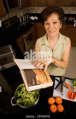 Ritratto di una donna anziana che tiene un libro di cucina nel cucina e sorridente Foto Stock