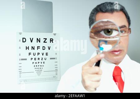 Ritratto di un medico maschio che tiene una lente di ingrandimento dentro davanti al suo occhio Foto Stock