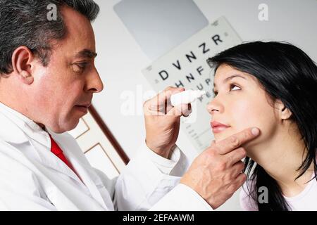 Profilo laterale di un medico maschio che mette collirio dentro Un occhio giovane womanÅ½s Foto Stock