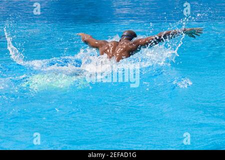 Vista posteriore di un uomo medio adulto che nuota la farfalla corsa in piscina Foto Stock