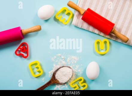 Divertente lezione di cucina per bambini concetto di bordo lotto di spazio per il testo. Uova, farina, spille, frese per biscotti a forma di lettera su fondo azzurro. Foto Stock