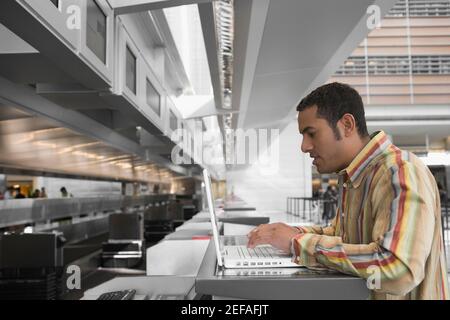Profilo laterale di un uomo medio adulto che utilizza un computer portatile in un aeroporto Foto Stock