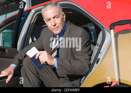 Ritratto di un uomo d'affari seduto in un taxi con la tenuta un passaporto e un biglietto aereo Foto Stock