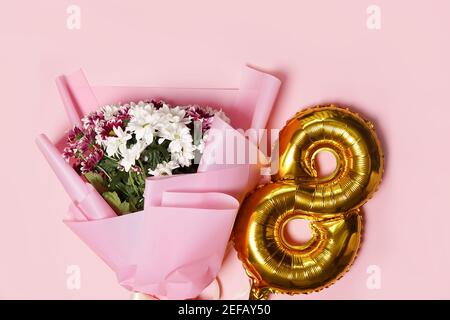 8 palloni di numero oro con bouquet di fiori rossi e bianchi. sfondo rosa. Festa della donna e 8 marzo Concept. Biglietto d'auguri Foto Stock