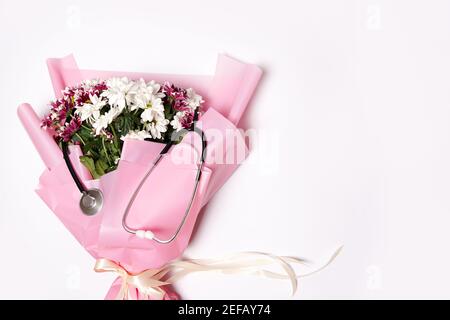 bouquet di fiori e stetoscopio su sfondo bianco. Giornata nazionale del medico. Buon giorno dell'infermiera. Vista dall'alto con spazio per la copia Foto Stock