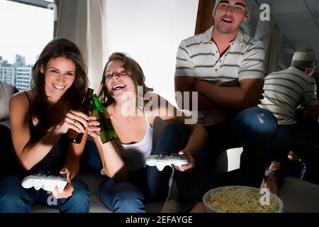 Due giovani che tostano con bottiglie di birra e una giovane uomo che sta accanto a loro Foto Stock