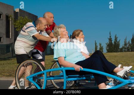Due donne anziane che siedono su un quadriciclo e due senior uomini che lo spingono Foto Stock