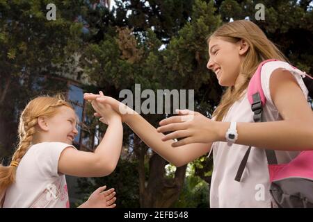 Vista ad angolo basso di due studentesse che giocano il gioco di aggrappamento e. sorridente Foto Stock