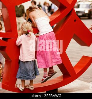 Vista posteriore di due ragazze che arrampicano una scultura a cavallo dondolante, Venezia, Veneto, Italia Foto Stock