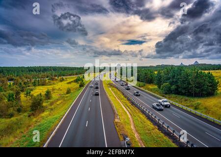 Queensland, Australia - Auto che si muovono lungo Bruce Hwy con le montagne Glass House sullo sfondo Foto Stock