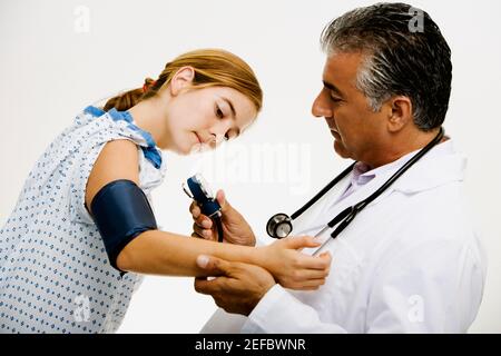 Profilo laterale di un medico di sesso maschile che misura la pressione sanguigna di una giovane donna Foto Stock
