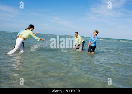 Profilo laterale di due coppie mid adult che spruzzi d'acqua sulla spiaggia Foto Stock