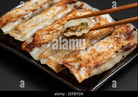 Materiale di gnocchi tradizionali cinesi fritti (anche chiamato gyoza, adesivo pentola) su sfondo nero con bastoncini. Foto Stock