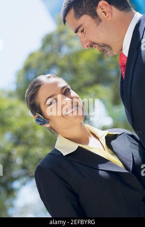 Ritratto di una donna d'affari che indossa un dispositivo a mani libere con un uomo d'affari sorridente accanto a lei Foto Stock