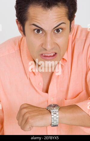 Ritratto di un giovane che fa un volto dopo il controllo il tempo sul suo orologio da polso Foto Stock