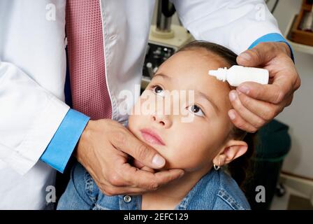 Vista in sezione intermedia di un medico che mette gli occhi gocce dentro Un occhio girlÅ½s Foto Stock
