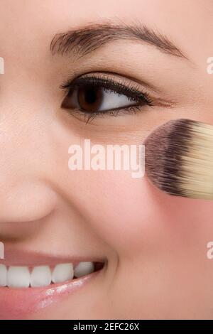 Primo piano di una giovane donna che applica make-up e sorride Foto Stock