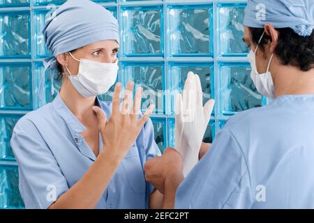 Chirurgo maschile regolazione di un guanto chirurgico di una chirurgo femminile Foto Stock