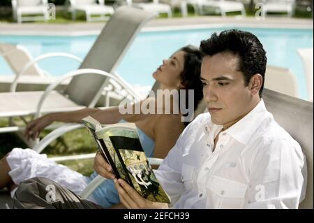 Profilo laterale di un giovane che legge un libro con una giovane donna seduta accanto a lui Foto Stock