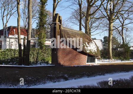 Piccola casa, fienile a forma di barca con tetto di paglia nel villaggio olandese di Bergen in inverno con neve. Alberi, cielo blu. Olanda, febbraio Foto Stock