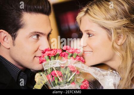 Primo piano di una giovane coppia che si guarda l'un l'altro con un mazzo di fiori tra loro Foto Stock