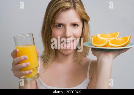 Ritratto di una ragazza adolescente che tiene un piatto di arance e un bicchiere di succo d'arancia Foto Stock