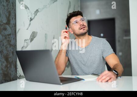 Uomo serio che indossa gli occhiali calcolando le fatture o le tasse domestiche, le spese della famiglia, usando il laptop e la calcolatrice nella cucina moderna Foto Stock