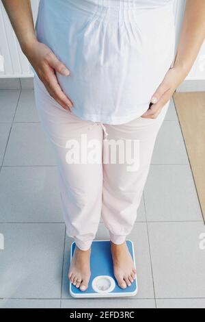 Vista in sezione bassa di una donna incinta in piedi su a. bilancia di pesatura Foto Stock