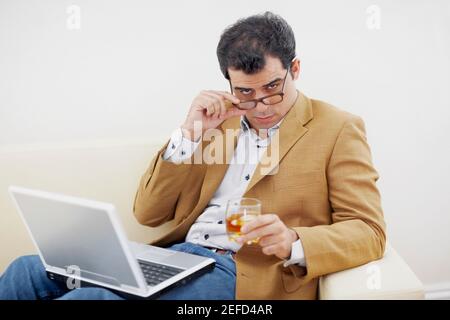 Ritratto di un uomo medio adulto che tiene un bicchiere di vino e guardando sopra gli occhiali Foto Stock