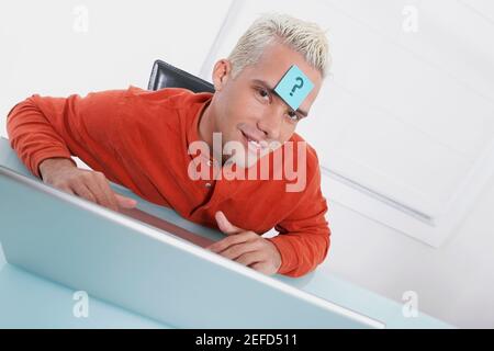 Ritratto di un giovane che usa un computer portatile con un nota adesiva sulla fronte Foto Stock