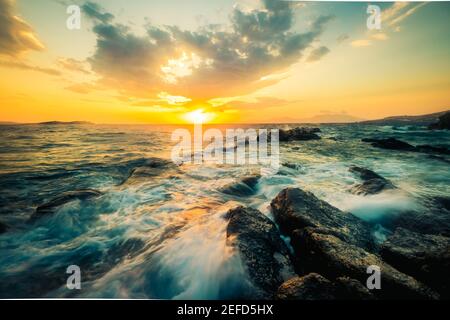 Bella stagione con rocce e onde al tramonto Foto Stock