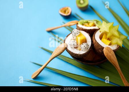 mescolare la frutta esotica in conchiglie di cocco con cucchiai Foto Stock