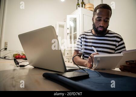 Un giovane studente di sesso maschile seduto al tavolo con è portatile, prende appunti sull'ordine del giorno. Foto Stock
