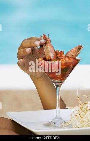 Primo piano di una mano di personÅ½s che raccoglie un gamberetto da un cocktail di gamberi Foto Stock