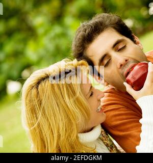 Primo piano di una giovane donna che alimenta una mela ad un uomo adulto medio Foto Stock