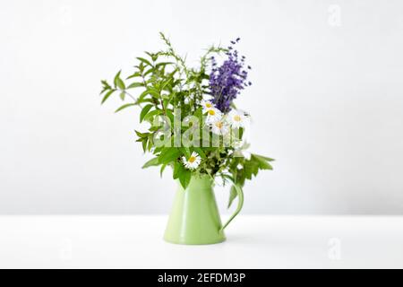 mazzo di erbe e fiori in caraffa verde sul tavolo Foto Stock
