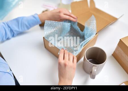 consegna la tazza di imballaggio alla scatola del pacco presso l'ufficio postale Foto Stock